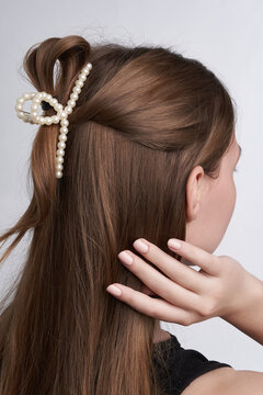 Close-up shot of a young woman with straight hair styled in a pearl claw clip. A girl with her back to camera showcasing claw clip hairstyle on a gray background.