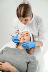 Beauty specialist in blue gloves makes a facial procedure for a girl with a smile