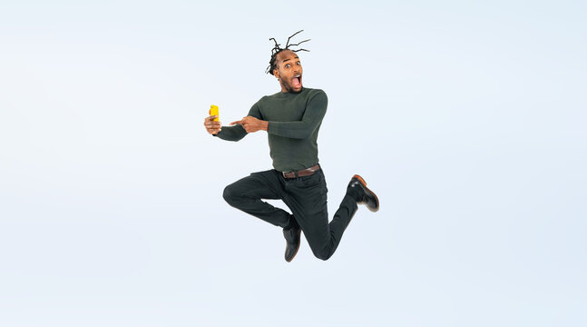 Full body photo of a Black man jumping while looking at his smartphone