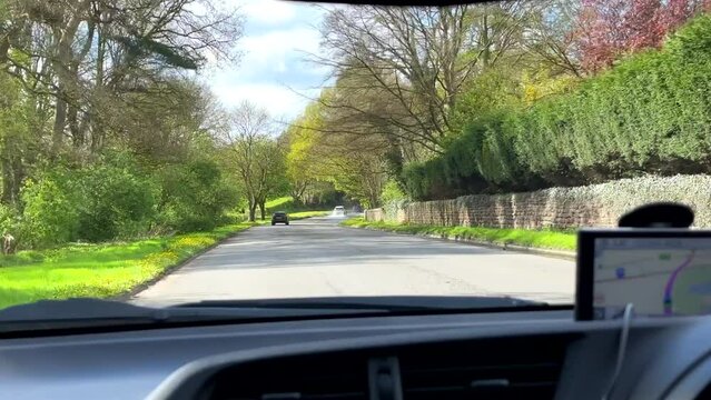 Car dashboard view driving on Warrington Road, A50 in Cheshire in a beautiful blooming springtime landscape; driver using sat nav navigation device for directions mounted on windscreen.