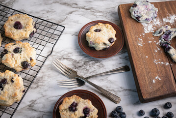 Freshly baked blueberry biscuits, scones, marbled background, wooden cutting board and plates.