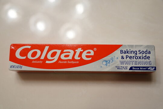 A box of a tube of Colgate Baking Soda and Peroxide Whitening Toothpaste sitting next to an Aim toothbrush in the bathroom.