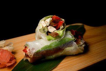 Vegetables rolls on a thick light wood board on a black background with ginger and wasabi