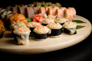 Sets of sushi on a round wooden board on a dark black background