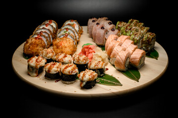 Sushi on a green leaf stuffed with rice, salmon, cheese, eel, shrimp, avocado on a round board - 791709171