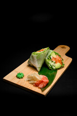 Wooden board with rolls with red fish and vegetables on a green leaf