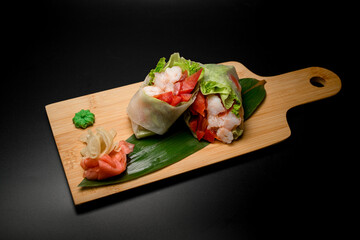 Appetizer rolls with seafood on a green leaf on a big board on a black background