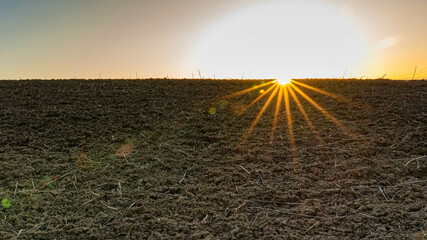 Ein Sonnenuntergang über einem frisch gepflügten Feld, mit leuchtenden Strahlen und einem Himmel...