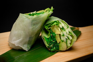 Vegetables rolls on a green leaf on a wood stand on a black background - 791716573
