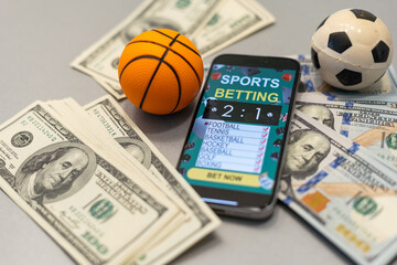 Smartphone with gambling mobile application and basketball ball with money close-up. Sport and...