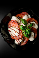 Black dish with soft cheeses and tomatoes with spices and soy sauce on a black background