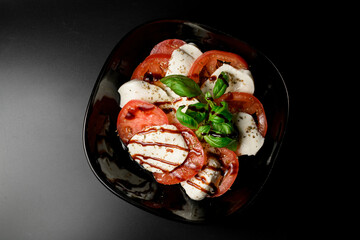 Black bowl with tomatoes and white cheese with spices and soy sauce