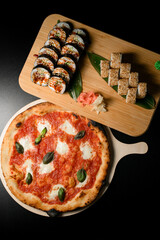 Pizza and sushi sets on a wooden boards on a dark black background