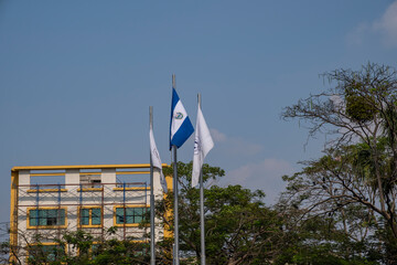 Flags of El Salvador and the capital city San Salvador waving against blue sky in city historical...