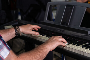 A close-up of a man's hands playing an electric organ. His fingers move swiftly across the...