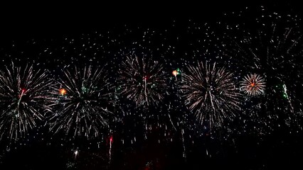 A massive firework bursts in the dark sky, creating a spectacular display of lights and colors