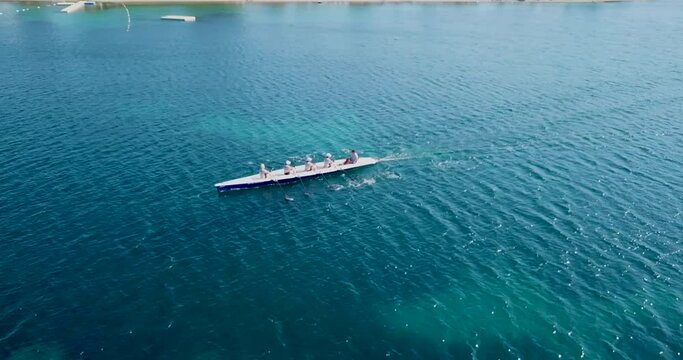 Racing coxed team aerial drone footage of a sports canoeing competition, athletes synchronising their movements in a calm, deep emerald sea. Teamwork concept in 4K resolution. Front high angle view.