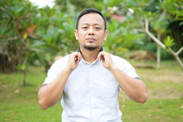 Asian male model wearing white shirt is sitting with facial expression in nature