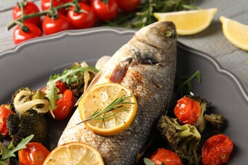 Baked fish with vegetables, rosemary and lemon on grey wooden table, closeup