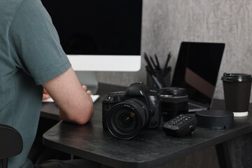 Photographer working on computer at dark table with camera, closeup
