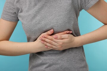 Woman suffering from stomach pain on light blue background, closeup
