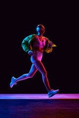 Dynamic image of sportive young girl in sportswear, jacket and headphones training, running on...
