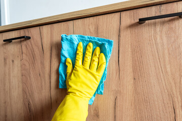 woman with yellow gloves wipes wooden table surface