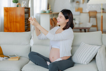Young Asian happy pregnant woman is sitting and relaxing on bed and touching her back pain. Family...