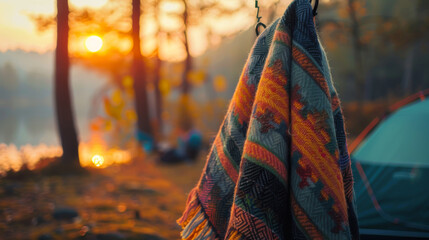 A colorful blanket is hanging from a tree next to a green tent - obrazy, fototapety, plakaty