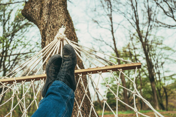 Man laying down and relaxing in back yard hammock attached to a tree, wearing jeans and dirty black sneakers