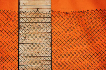 Chain link fence casting shadow over orange wall and doors shut with wooden planks - 791786780