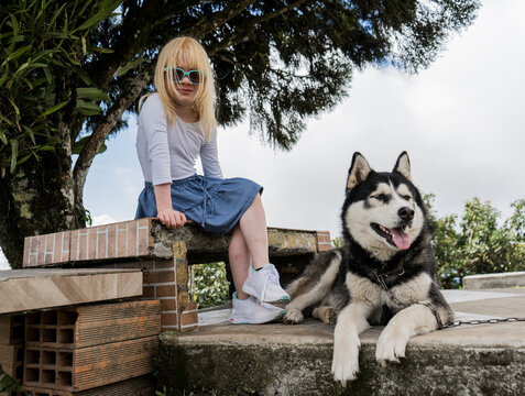 niña albina sentada en una banca del parque mientras esta en compañia de su perro 