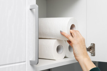 housewife takes out a roll of paper towel from the kitchen cabinet.