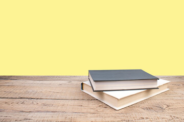 Composition with hardback books, fanned pages on wooden deck table and yellow background. Books stacking. Back to school. Copy Space. Education background.