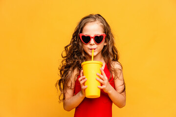 Little smiling beautiful girl in sunglasses and red swimsuit drinking lemonade through a tube on...