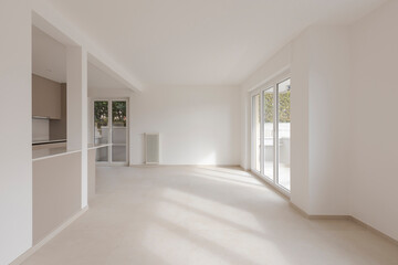 Large empty dining room with windows to the right and kitchen to the left.  It is a new house with white walls