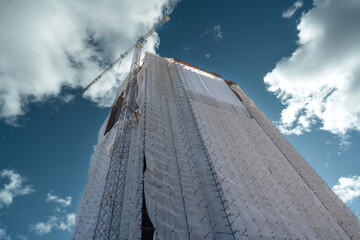 A tall building under renovation is covered with a protective cloth.