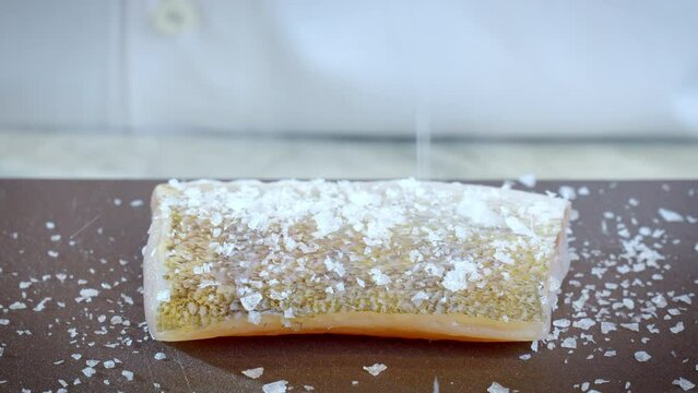 The cook prepares zander, pikeperch fillet. Raw zander is sprinkled with salt before frying. Slow motion, 4k video.