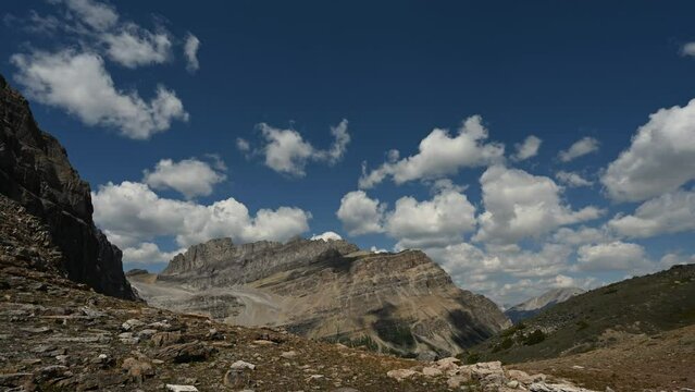 Time lapse of clouds building above majestic mountains in Banff National Park. A hiker scurries through the frame at the beginning of the clip.
