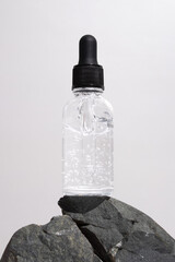 Transperent glass dropper bottle with a pipette on stones, grey background. Natural cosmetics concept, natural essential oil.