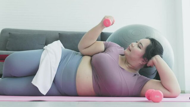 chubby woman lies down and lifts dumbbells. Exercise