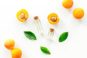 Apricot kernel oil among apricots and leaves on white background top view pattern