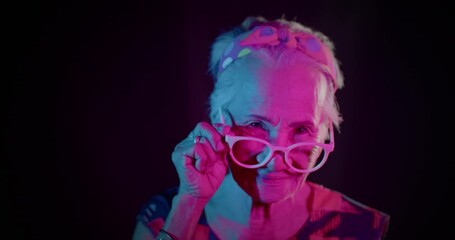 Slow motion : A funny smiling Asian woman who is an elderly woman, likes to have fun, be in a good sense of humor, showing off her acting to the people amidst the colorful of festival light.  - Powered by Adobe