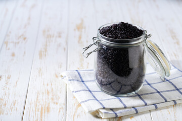 raw black rice in glass storage jar on a white wooden table.