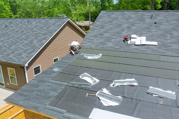 Using an air nail gun, professional roofing contractors install new asphalt bitumen shingles on...