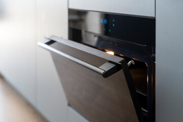 Modern electric oven with opened door integrated in kitchen cabinet