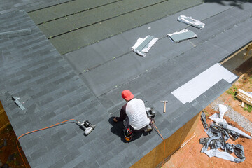 With assistance an air nail gun, professional roofing contractor installed new asphalt bitumen...