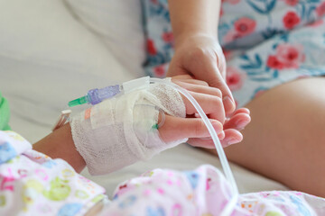 Mother holding child hand with saline IV solution in hospital - 791833341