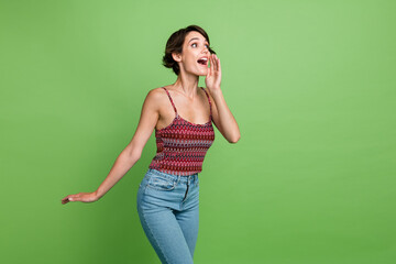 Photo of funny lovely positive girl wear trendy clothes hand mouth announces news look empty space isolated on green color background