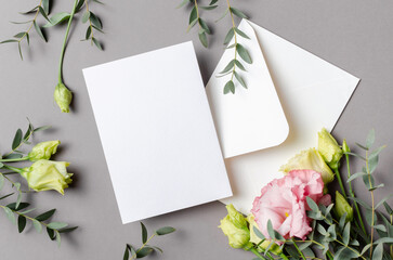 Wedding invitation card mockup with flowers and white envelope on grey, flat lay with copy space